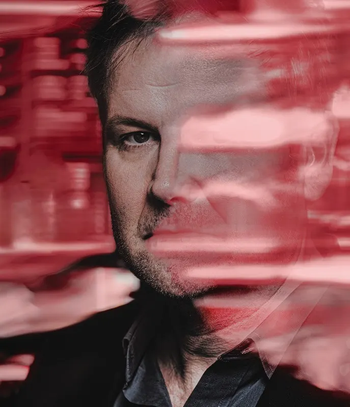 closeup of middle aged white man in black jacket, with his faced obscured and surrounded by red streaks of light