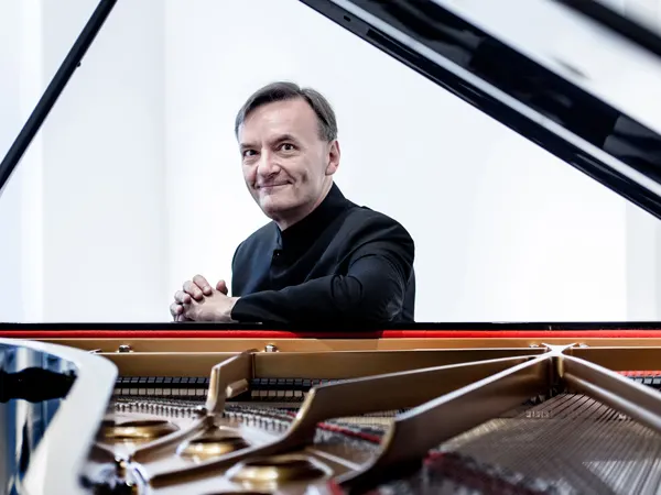 Sir Stephen Hough sits by a grand piano. He smiles.