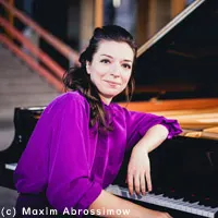 Yulianna Avdeeva sits in front of a grand piano. She wears a purple blouse.