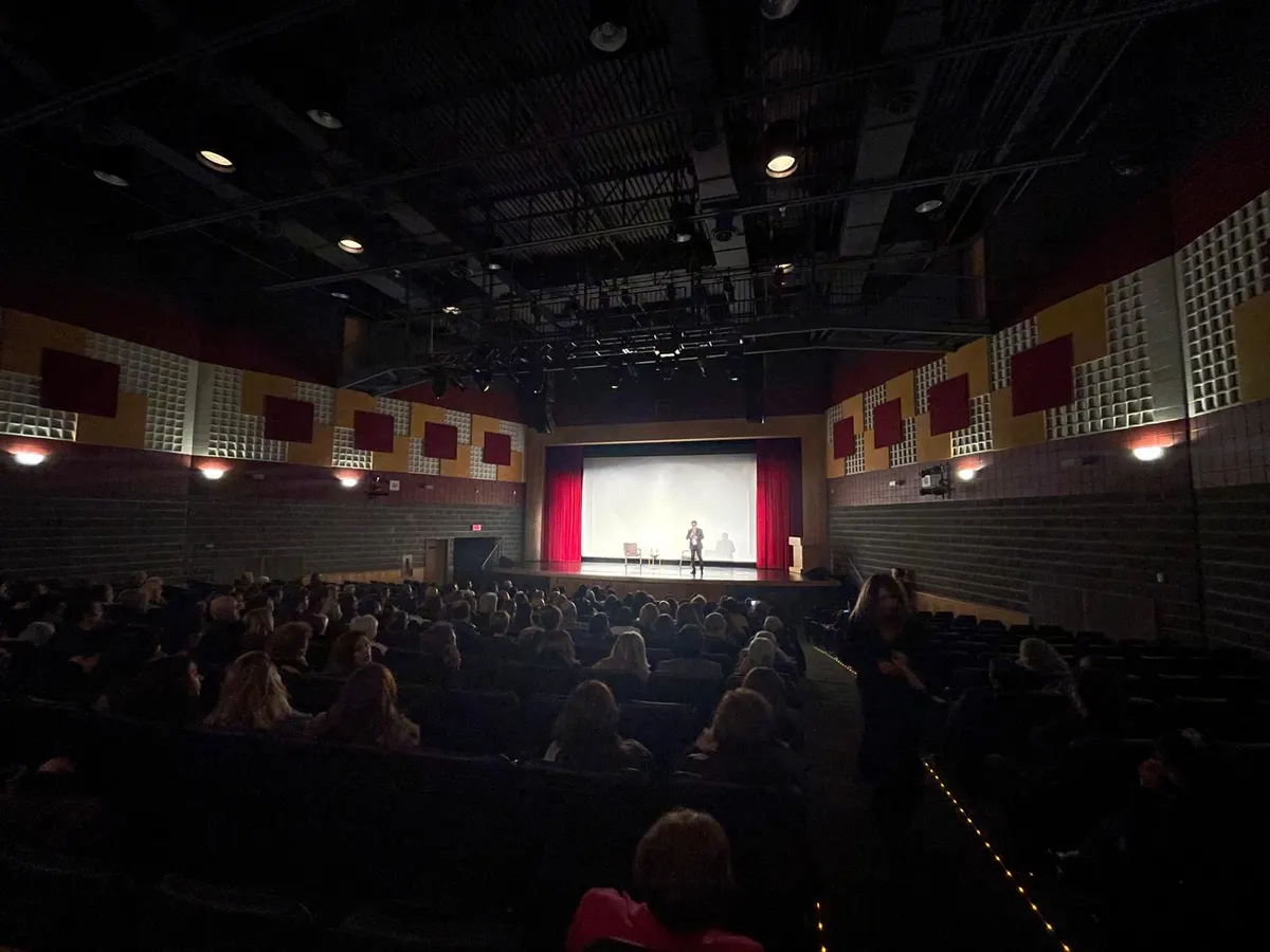 Audience seated in the Hamazkayin Theatre as a speaker addresses the crowd onstage in front of a projection screen.