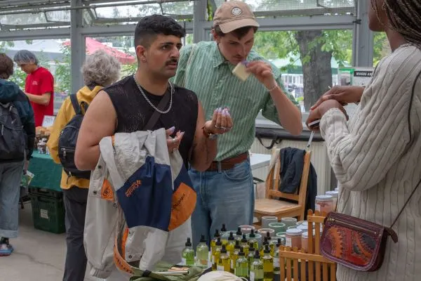 two customers trying beauty products and engaging with a vendor at the farmers' market