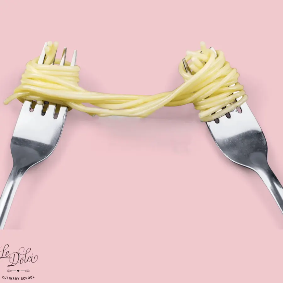 Pink background with two silver forks holding pasta between them