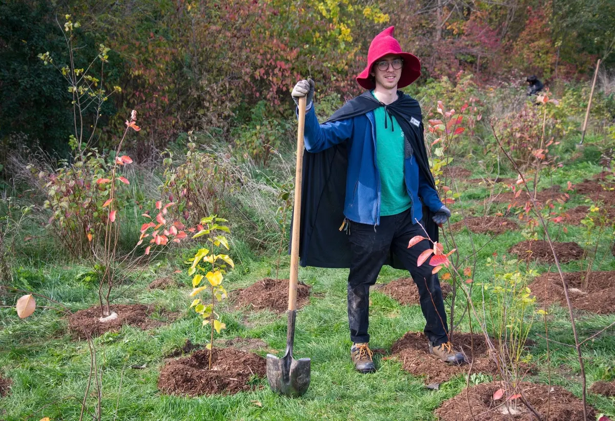 City staff wearing a wizard costume posing with newly planted trees and shrubs at Halloween planting event