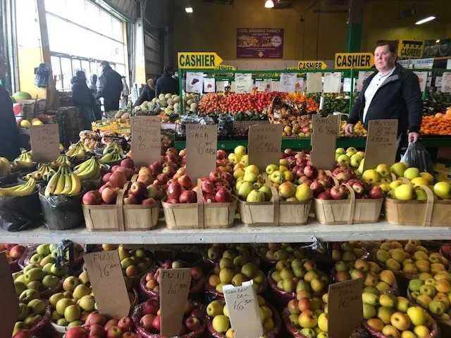 table with different types of apples in a display for sales, various signs in a busy market. Shopper