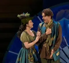Two people dressed in medieval clothing singing in front of a black background.