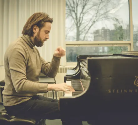 Daniil Trifonov plays the piano. He wears a moss green turtleneck.