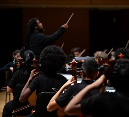 A group of young people play in an orchestra, dressed in black.