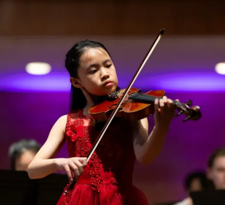 A young girl in a red dress plays the violin.