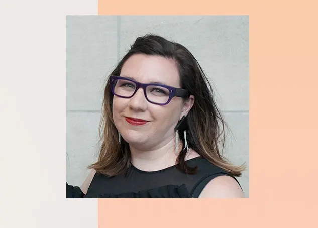 Alysa Procida in a black shirt and beige background. She wears purple glasses and red lipstick.