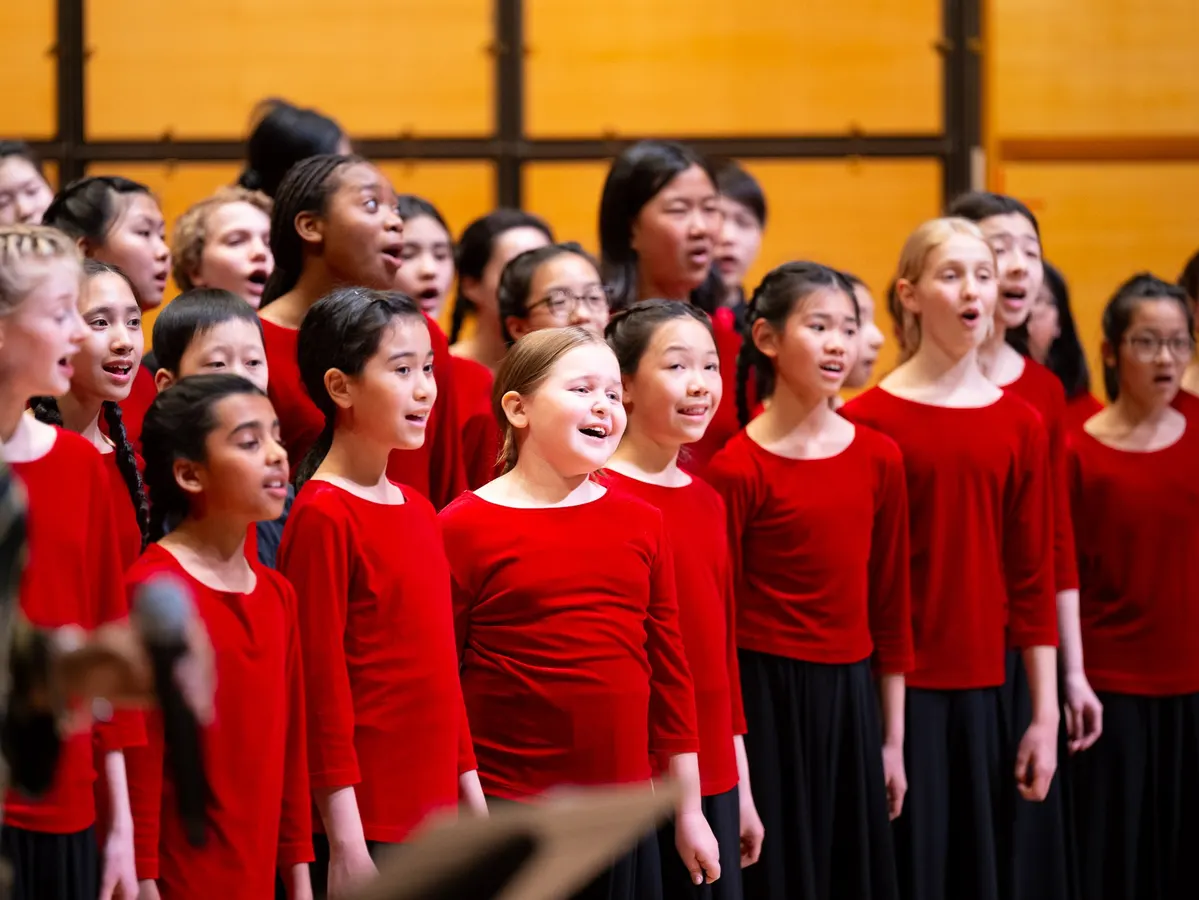 A children's choir wearing red tops are singing on stage