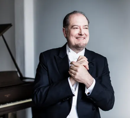 Garrick Ohlsson stands in a suit, clasping his hands.